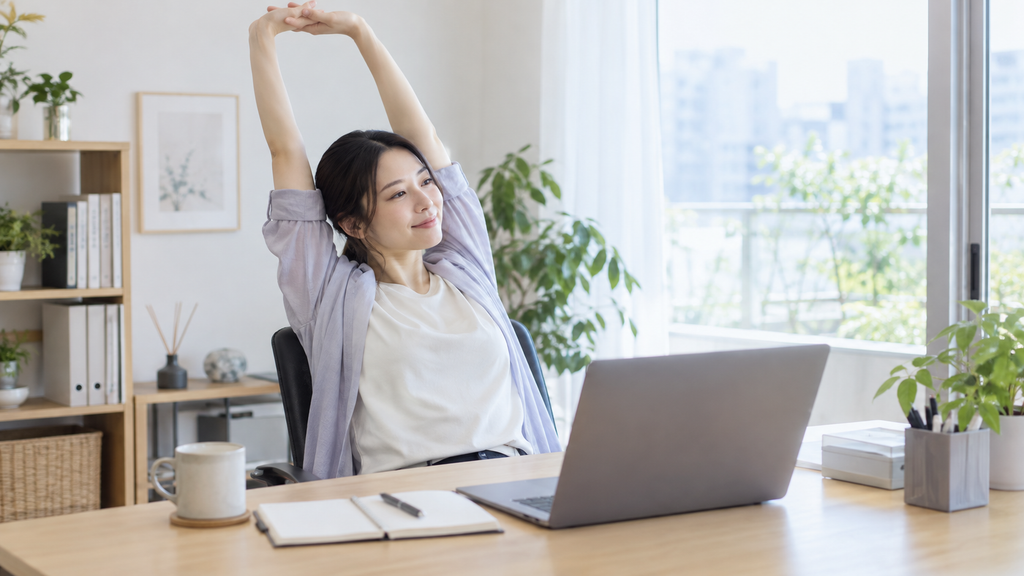 デスクワークの合間に背伸びをする女性の様子